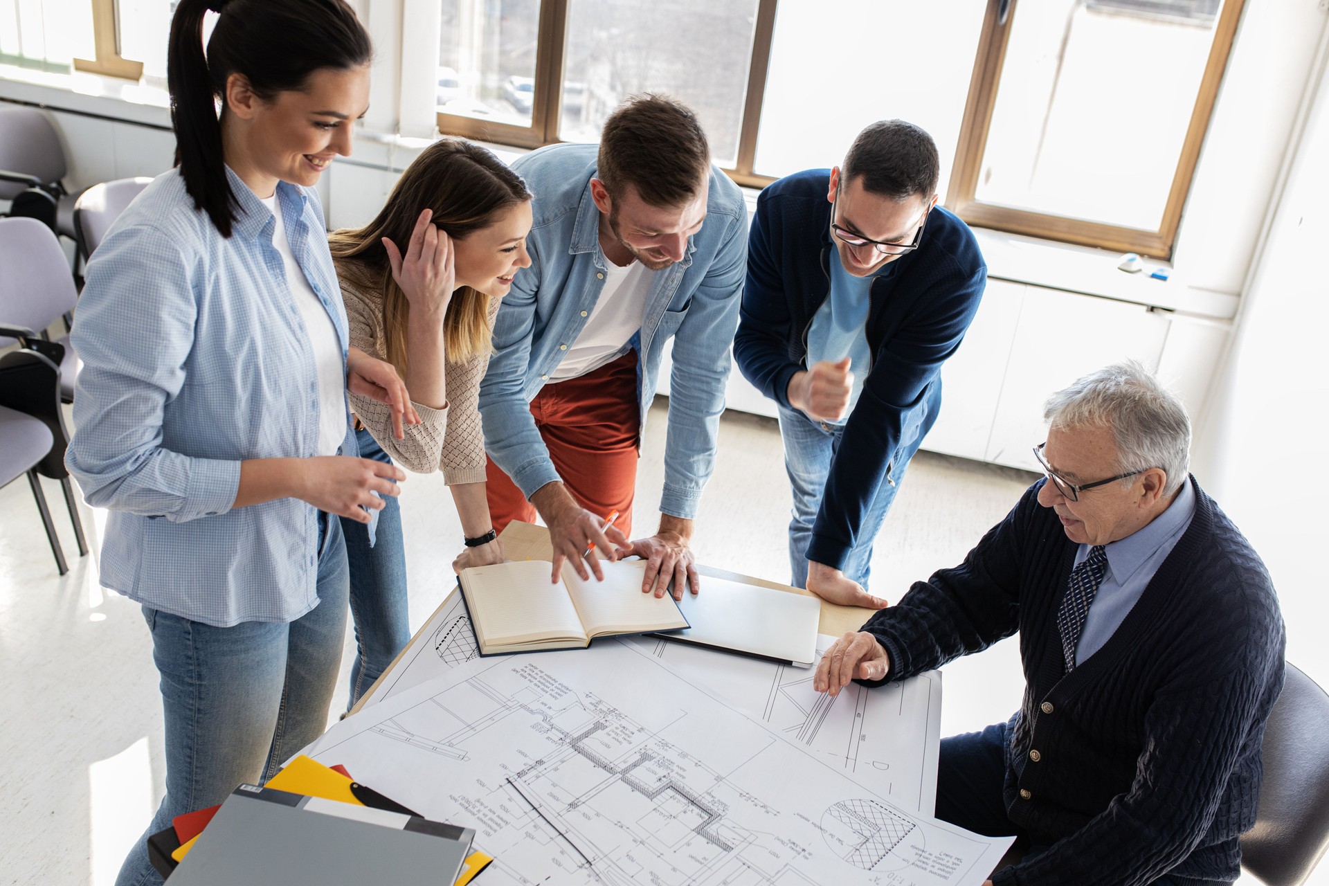 College architecture professor examining blueprint with group of his students.